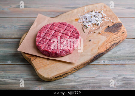 Raw hamburger di manzo con spezie su un tagliere di legno Foto Stock