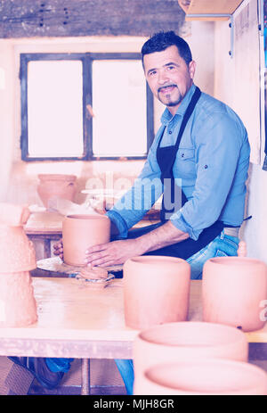 Sorridente uomo anziano rendendo pot con ruota di ceramiche in studio Foto Stock