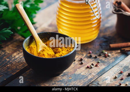 Curcuma in polvere in un recipiente nero con spezie su tavola in legno rustico Foto Stock