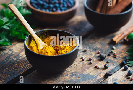 Curcuma in polvere in un recipiente nero con spezie su tavola in legno rustico Foto Stock