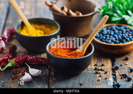 Piccole ciotole riempite con spezie su tavola in legno rustico. Vari ingredienti sul tavolo. Foto Stock