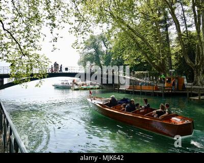 Vecchia barca in legno che porta un piccolo gruppo di persone che passa sotto il ponte pedonale sulla via di uscita nel lago di Annecy, Annecy, Francia Foto Stock