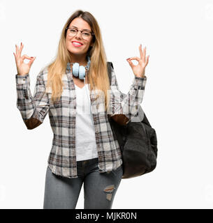 Giovane studente donna con le cuffie e uno zaino facendo segno ok gesto con entrambe le mani che esprimono la meditazione e relax Foto Stock