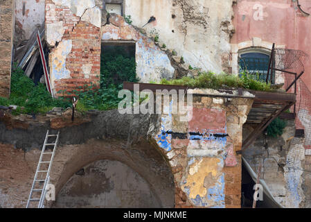 Rovine di vecchi muri di mattoni sono rosa, lo stucco è caduta, tra la devastazione non ci sono verdi arbusti ed erba, vicino alla parete una scaletta in legno sta Foto Stock