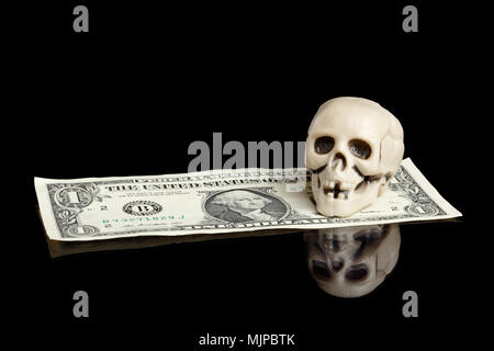 Un piccolo teschio di plastica su un dollaro banconota isolati su nero. Foto Stock