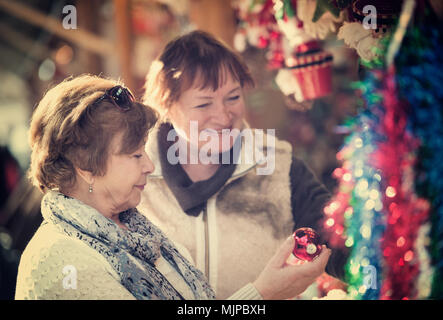 Allegro senior donne camminando sul mercato di Natale e la scelta di gioielli. Focus sulla sinistra donna Foto Stock