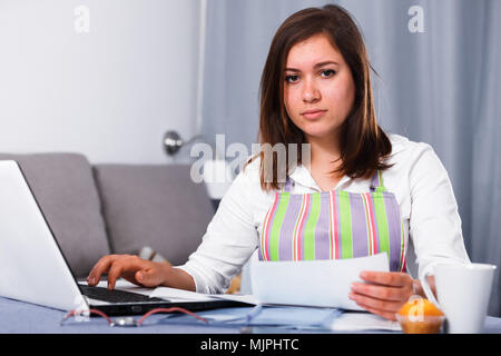 Giovane donna navigando attraverso utili suggerimenti per la cottura in Internet Foto Stock