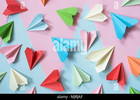 Colorati aeroplani di carta sul rosa pastello blu e sfondo colorato. l'infanzia,la libertà e il concetto di diversità Foto Stock