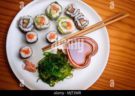 Alta Vista angolata di un piatto di sushi e bacchette. Un cuore a forma di vaso vetroso con salsa di soia. Foto Stock