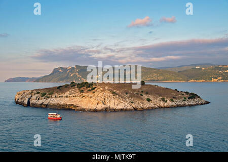 Una piccola isola rocciosa tavsan circondata da calme acque blu al tramonto, caratterizzata da una barca rossa. Costa del Mar Nero in Turchia, Amasra, Foto Stock