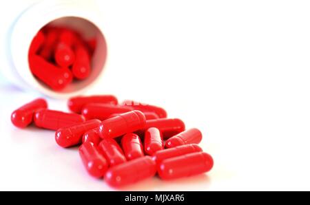 Le capsule di rosso versato fuori da un contenitore su sfondo bianco. Foto Stock