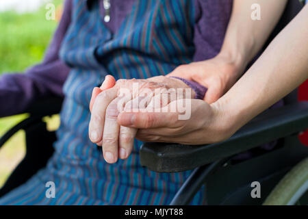 Chiudere l immagine del caregiver holding anziani donna mani di scuotimento, seduto in una sedia a rotelle - Morbo di Parkinson Foto Stock