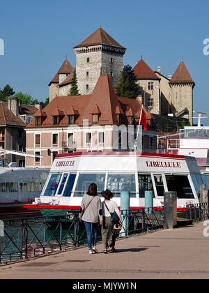 Due donne a piedi lungo la sponda del lago, passando per le imbarcazioni turistiche, con il castello di Annecy in aumento in background, Annecy, Francia Foto Stock