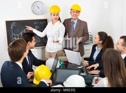 Energico professionisti positivo con i laptop e caschi con riunione di lavoro Foto Stock