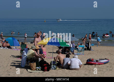 Le persone che si godono il sole in spiaggia Branksome, Poole, come per i fanatici del sole sono impostati a sizzle nella primavera canicola, con lunedì festivo previsioni per essere il più caldo da quando sono iniziate le registrazioni. Foto Stock