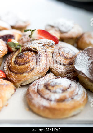 Una selezione di pane appena sfornato e smerigliati pasticcini danesi e ciambelle dolci su un business prima colazione a buffet spolverati con zucchero a velo e guarnita con s Foto Stock