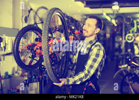 Uomo sorridente master stabilisce una ruota di bicicletta nel suo laboratorio Foto Stock