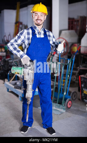 Adulto lavoratore cominciando a lavorare con martello da demolizione in officina Foto Stock