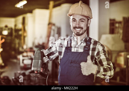 Sorridente uomo di lavoro mettere in pratica le sue abilità con il seghetto alternativo di potenza in un workshop Foto Stock