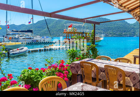 La vista su yacht nel cantiere navale e il verde delle montagne dalla terrazza estiva del cafè sulla riva della baia di Kekova, Kalekoy, Turchia. Foto Stock