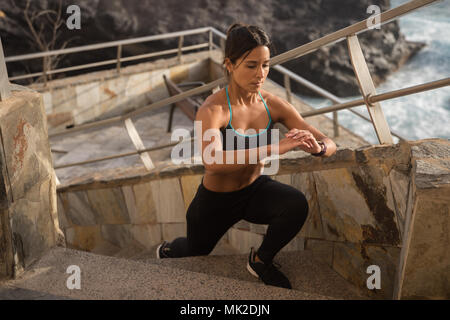 Un forte cercando giovane donna facendo esercizi su un set di scale con il sole sulla sua pelle e il mare al di sotto di Foto Stock