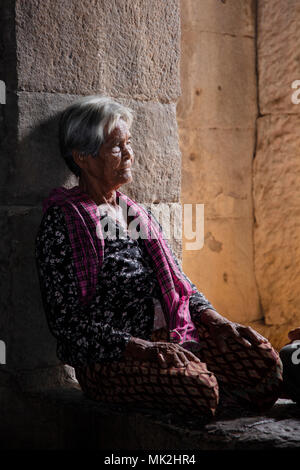 Una donna anziana appoggiata contro la porta di pietra del tempio di Ta Prohm a Takeo, in Cambogia Foto Stock