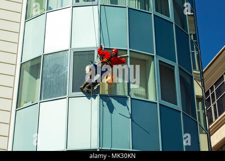 Lavoratore in un casco lava la finestra di un edificio alto dall'esterno, appeso a una fune Foto Stock