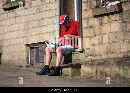 New Mills High Peak DERBYSHIRE REGNO UNITO 7 Maggio 2018 Un anziano gentiluomo si siede sul suo gradino anteriore leggendo il giornale del mattino su un molto caldo lunedì festivo. Credito: Giovanni friggitrice/Alamy Live News Foto Stock