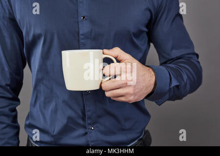 Bel uomo barbuto con elegante capelli barba e baffi sulla faccia gravi in camicia bianca di contenimento della tazza o tazza alta bere il tè o caffè in studio su sfondo grigio Foto Stock