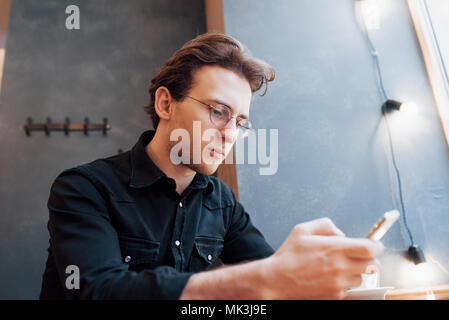 Ritratto bello uomo barbuto cuffie guardando un video telefono mobile moderno studio loft.uomo seduto nella sedia d'epoca,tenendo lo smartphone e rilassante.orizzontale, film, effetto bokeh di fondo Foto Stock