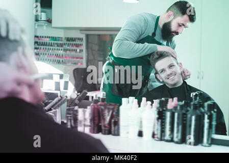 Friendly guy stilista creazione nuova forma per la barba di client al salone di parrucchiere Foto Stock