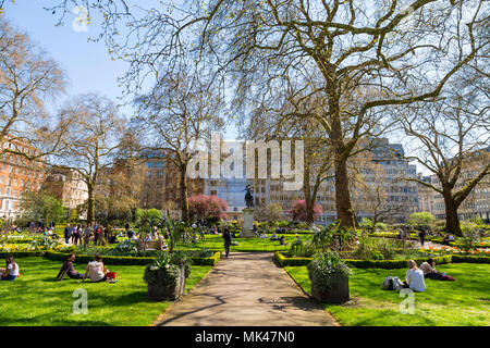 La Gente seduta sul prato e mangiare il pranzo in un piccolo parco cittadino, St James's Square Garden, Londra, Regno Unito Foto Stock