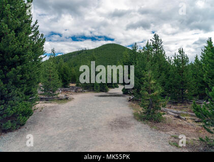 Strada sterrata nel bosco con alti collina verde in background sotto il cielo nuvoloso con patch di blu. Foto Stock