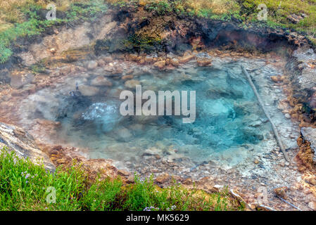 Il gorgogliamento primavera calda con un profondo colore blu nel campo con erba verde intorno a. Foto Stock