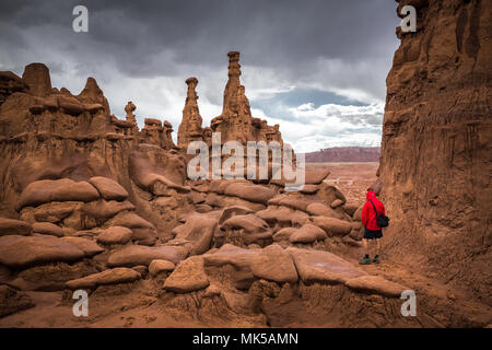 Vista panoramica di un escursionista in giacca rossa in piedi di Goblin Valley State Park in mezzo a bellissimi hoodoos formazioni arenarie, Utah, Stati Uniti d'America Foto Stock