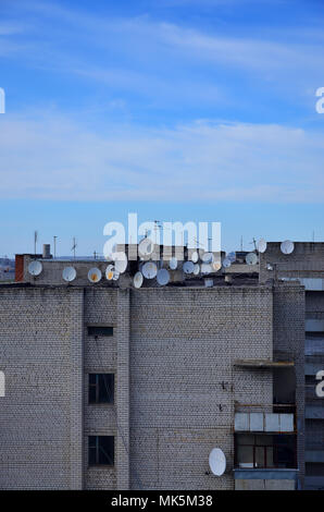 Un sacco di televisione via cavo e satellite antenne sono collocate sul tetto di un edificio a più piani sotto un cielo blu. Bianco vecchia televisione satellitare Foto Stock