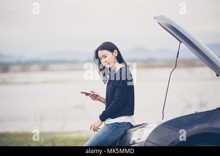 Donna asiatica utilizzando il telefono cellulare mentre cercano e sottolineato uomo seduto vettura dopo un guasto su strada Foto Stock