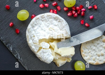 Formaggio Camembert, coltello, cracker e i semi di melograno sul formaggio scheda di ardesia Foto Stock