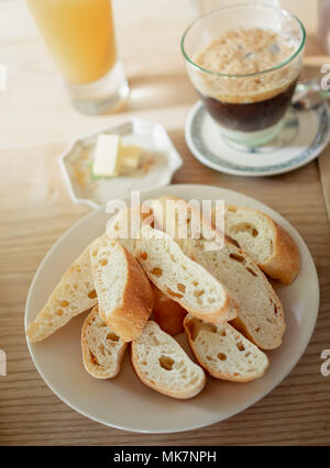 Francese croccante fetta di pane, caffè, succo d'arancia, il burro sul tavolo di legno per la colazione al mattino Foto Stock