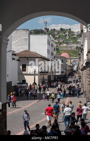 Pedoni su una strada nel centro storico della città di Quito, Ecuador. La Virgen de Quito statua su El Panecillo Hill è in background. Foto Stock