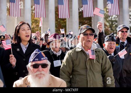 I partecipanti della 64a veterani nazionale giorno osservanza onda bandiere degli Stati Uniti presso il Cimitero Nazionale di Arlington in Arlington, Virginia, nov. 11, 2017. Più di 200 persone hanno partecipato alla manifestazione per celebrare e onorare i membri del servizio che hanno servito e attualmente servire. Gli Stati Uniti Air Force per band da concerto è stato presentato in osservanza. (U.S. Air Force foto di Airman 1. Classe Valentina Lopez) Foto Stock