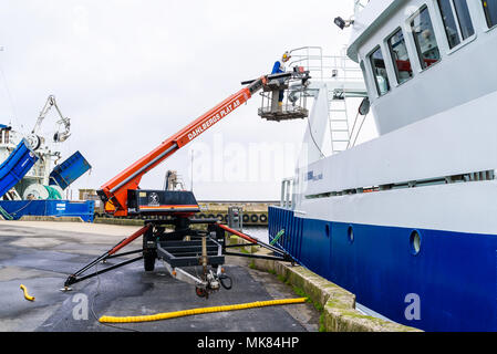 Simrishamn, Svezia - 27 Aprile 2018: documentario di viaggio della vita quotidiana e l'ambiente. Persona nella piattaforma di lavoro aerea (AWP) usando una smerigliatrice angolare Foto Stock