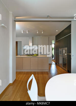 Scatti di interni di una cucina moderna con cucina isanad in primo piano il bianco tavolo da pranzo il pavimento è in legno Foto Stock