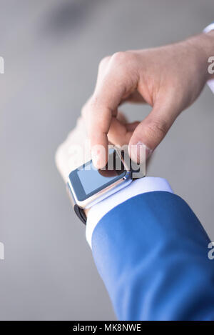 Persona che utilizza lo scooter elettrico e un smartwatch nel parco e sulla strada in una giornata di sole, con effetto bokeh di fondo. Foto Stock