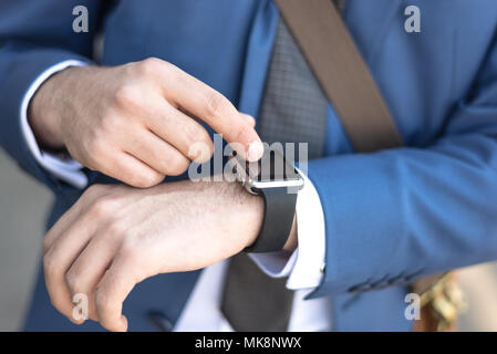 Persona che utilizza lo scooter elettrico e un smartwatch nel parco e sulla strada in una giornata di sole, con effetto bokeh di fondo. Foto Stock