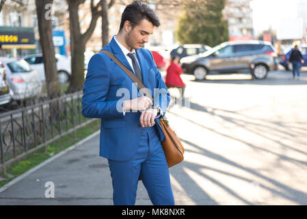 Persona che utilizza lo scooter elettrico e un smartwatch nel parco e sulla strada in una giornata di sole, con effetto bokeh di fondo. Foto Stock