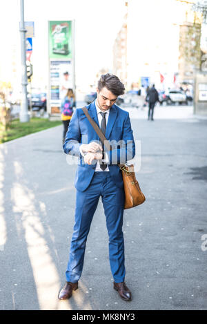 Persona che utilizza lo scooter elettrico e un smartwatch nel parco e sulla strada in una giornata di sole, con effetto bokeh di fondo. Foto Stock