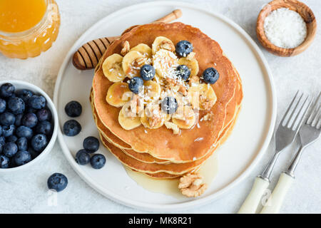 Gustosi pancake con banane, mirtilli, noci e miele sulla piastra bianca. Primo piano. Pila di Pancake fatti in casa. Frittelle il cibo della colazione Foto Stock