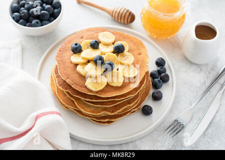 Frittelle pila con banana, mirtilli e miele. In casa frittelle americane sulla piastra bianca. La colazione concetto, composizione orizzontale Foto Stock
