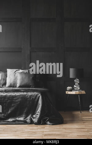 La Lampada sul tavolo di legno accanto al letto in moderna camera da letto nero interno con modanatura sulla parete Foto Stock